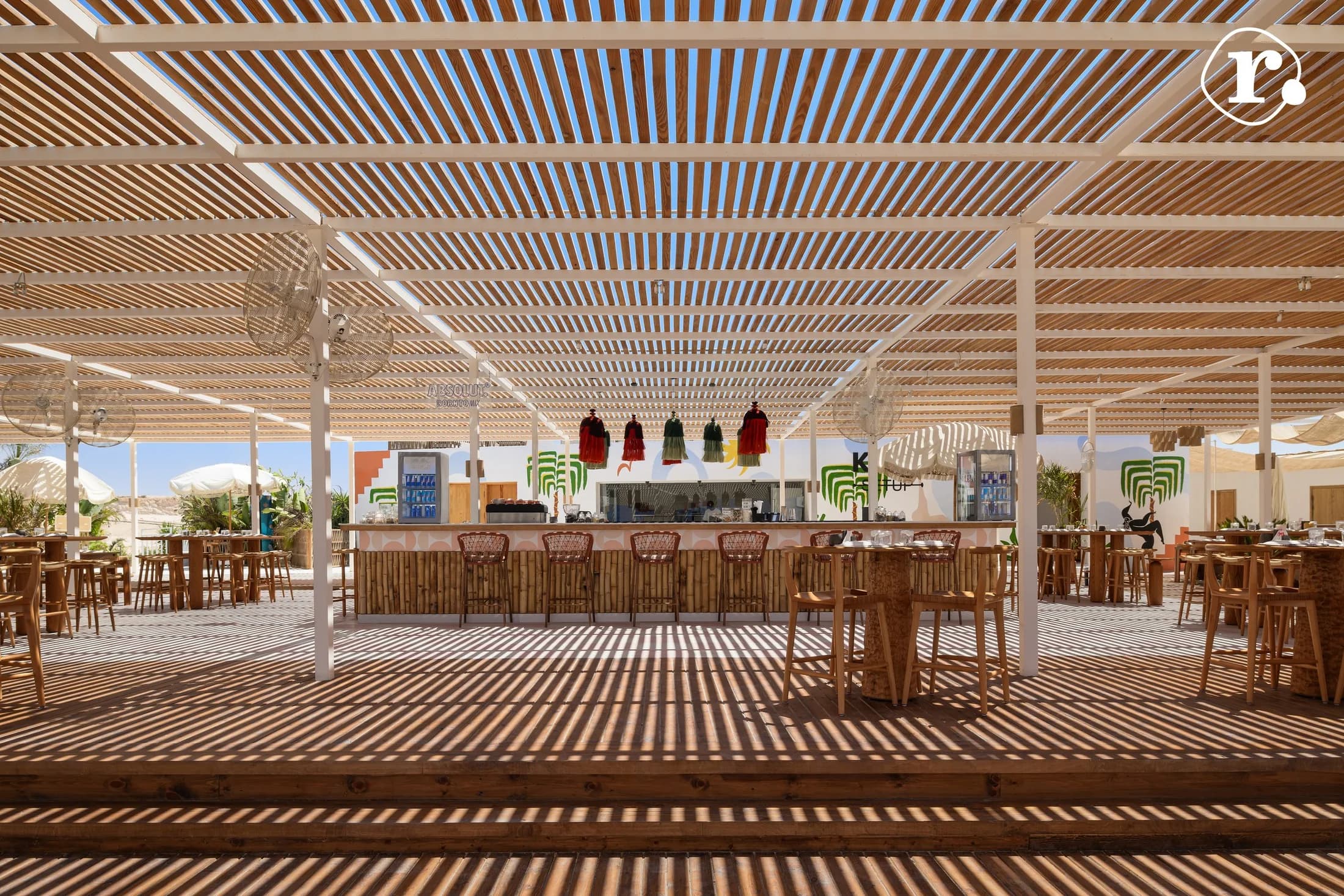 Open-air bar and timber pergola casting striped shadows across the floor
