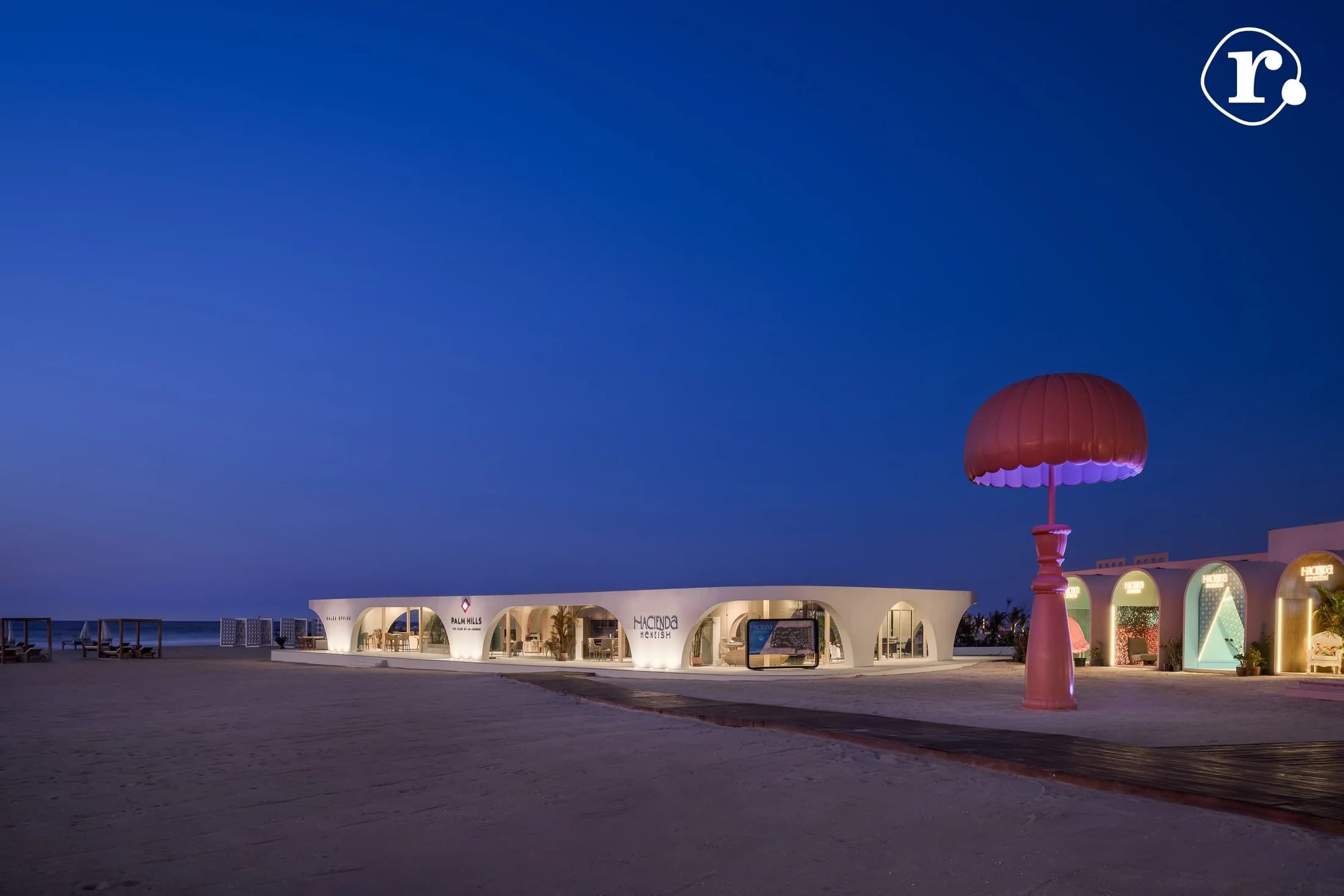 Wide view of the beachfront setting and lit pavilions at blue hour